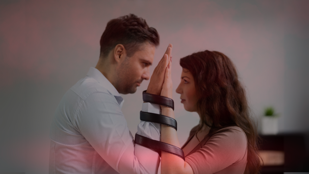 Casal se encara com as mãos unidas, amarradas por uma faixa preta, simbolizando desafios e conexões no relacionamento. A imagem transmite a ideia de laços emocionais fortes, mas também de obstáculos a serem superados juntos.