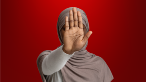 Mulher com expressão séria e mão contínua em sinal de pare, usa um hijab cinza claro, com fundo vermelho intenso, simbolizando alerta e proteção contra um falso pai de santo.