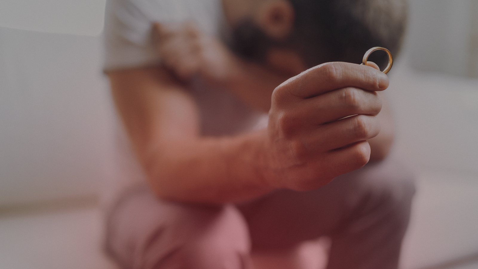Um homem segurando uma aliança de casamento em sua mão, enquanto parece abatido e pensativo, retratando um momento em que o casamento acabou de verdade.