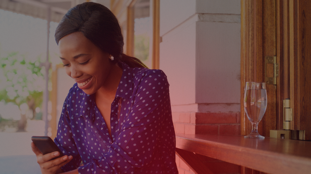 Uma mulher sorrindo enquanto olha para seu celular, transmitindo felicidade e entusiasmo ao receber uma mensagem ou ligação importante.

