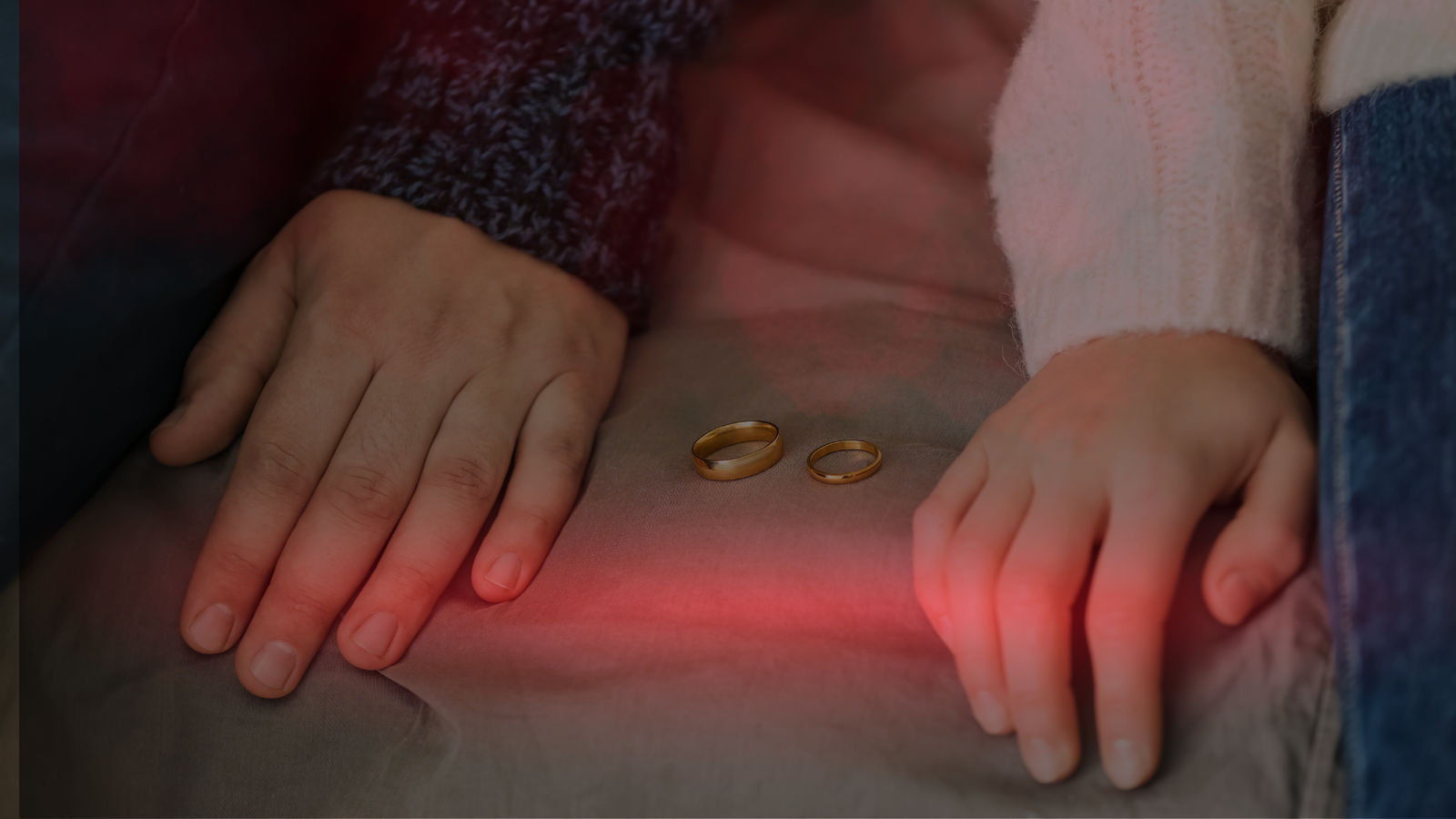 Mãos de um casal repousam sobre uma superfície com duas alianças entre elas, simbolizando um momento de crise no relacionamento. A imagem transmite sentimentos de crises no relacionamento