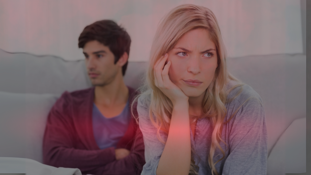 Casal sentado no sofá, demonstrando distanciamento emocional e frustração. A mulher aparenta estar pensativa e preocupada, enquanto o homem olha para o lado, sugerindo um momento de crise no relacionamento.
