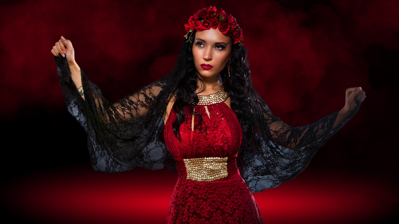 Mulher vestida de vermelho com detalhes dourados, usando uma coroa de rosas vermelhas e um manto preto rendado. Ela tem uma expressão séria e misteriosa, em um cenário de fundo vermelho com tons sombrios. Simbolizando quem é Pomba Gira