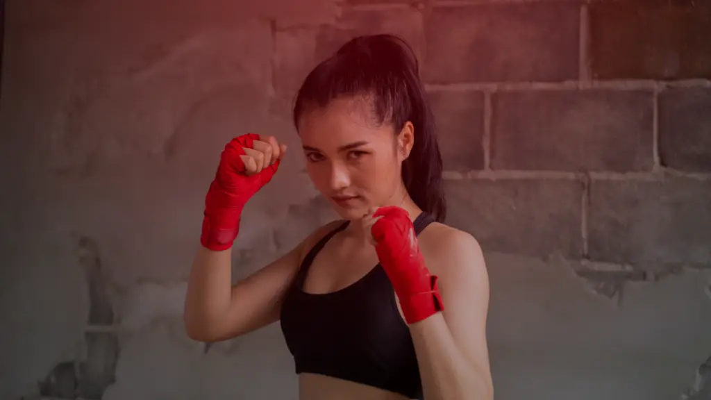 Mulher com expressão determinada em posição de luta, usando faixas vermelhas nas mãos, representando força, coragem e empoderamento feminino na prática do dia a dia.