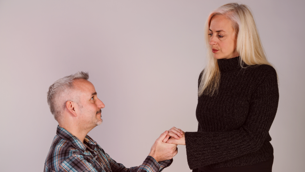 Homem ajoelhado segurando as mãos de uma mulher com expressão séria e distante, enquanto ela olha para ele sem demonstrar emoção. A cena simboliza a mudança de poder no relacionamento, destacando o impacto da valorização pessoal e da indiferença estratégica.