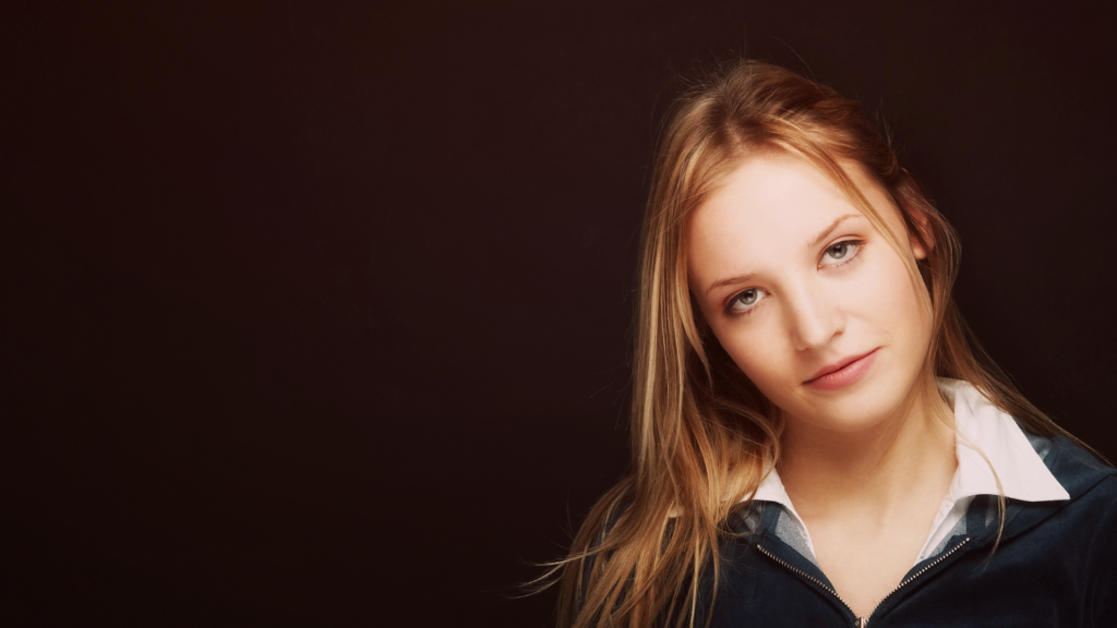 Mulher jovem com olhar sereno e expressão neutra, transmitindo um ar de desapego e indiferença. O fundo escuro destaca sua presença, criando um contraste que reforça a ideia de distanciamento emocional e mudança de postura.