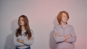 Casal jovem com os braços cruzados e expressão de afastamento emocional, representando a tensão em um relacionamento com pessoa de apego evitativo.