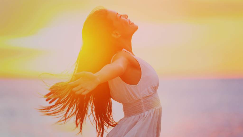 Mulher sorridente de braços abertos ao pôr do sol, representando liberdade, autoconfiança e empoderamento — essência do flerte feminino autêntico.