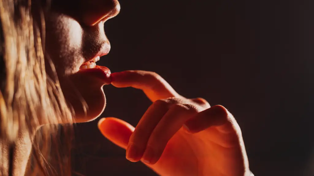 Close sensual de mulher tocando os próprios lábios com o dedo em uma atmosfera quente, representando o significado de sedução com desejo, provocação e intimidade.