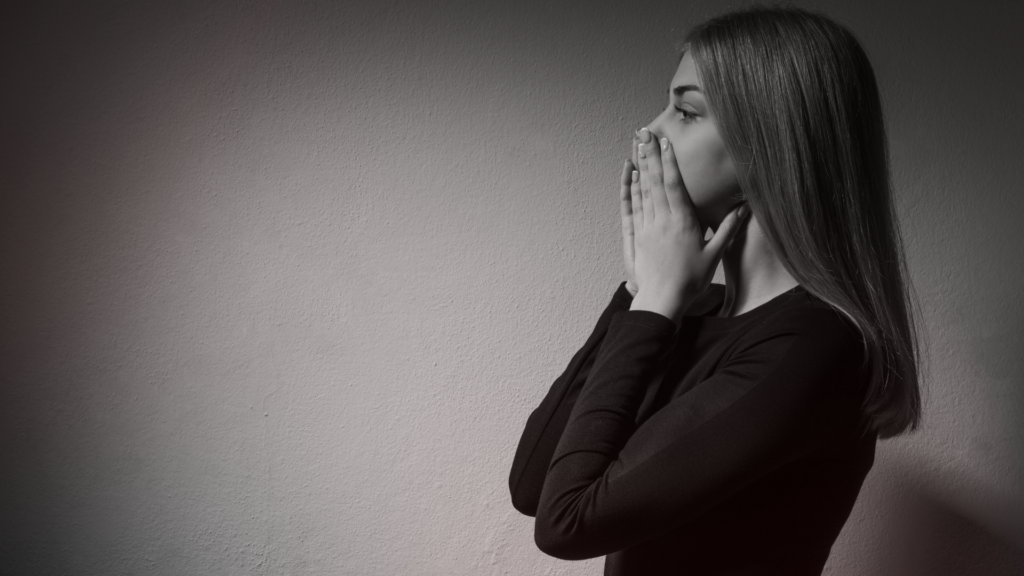 Mulher de perfil com expressão de preocupação, mãos sobre a boca, em ambiente escuro e silencioso — representando reflexão, dúvida e o peso emocional de relações que aprisionam.