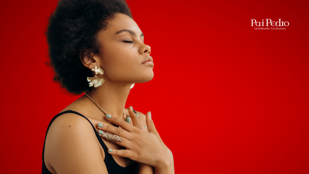 Mulher de olhos fechados com expressão serena, mãos cruzadas sobre o peito em gesto de conexão espiritual, diante de um fundo vermelho intenso. Ela transmite força, paz e introspecção.