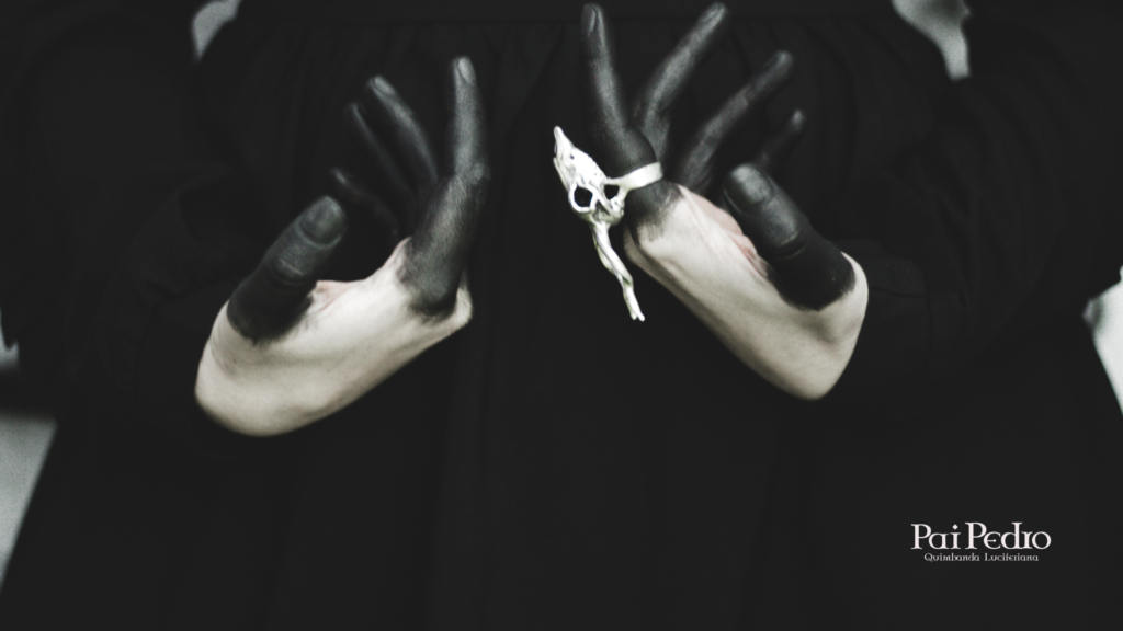 Mãos pintadas de preto em posição ritualística seguram um anel com crânio prateado, em gesto simbólico de respeito e concentração. A imagem remete à ética nos rituais da Quimbanda, onde a força espiritual caminha lado a lado com a responsabilidade e reverência.
