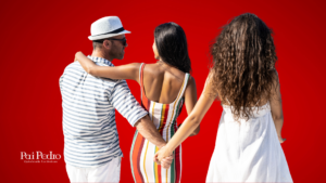 Homem de camisa listrada e chapéu caminha de braços dados com uma mulher de vestido colorido, enquanto segura escondido a mão de outra mulher de vestido branco. O fundo é vermelho intenso, transmitindo tensão e traição, Relacionamento Extraconjugal . No canto inferior esquerdo está o logotipo "Pai Pedro - Quimbanda Luciferiana".