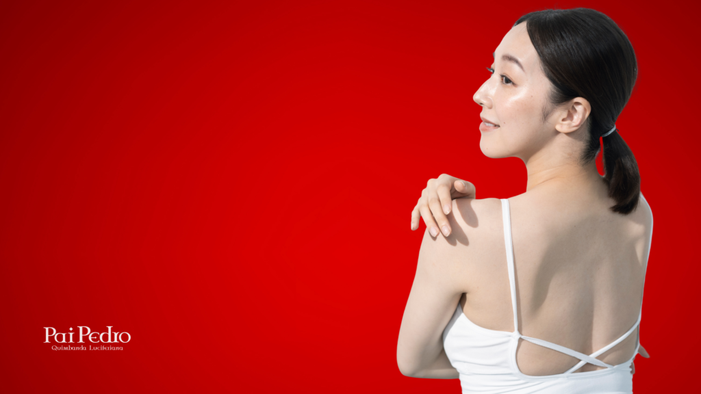 Mulher de costas com expressão serena, tocando suavemente o próprio ombro, em frente a um fundo vermelho vibrante. A imagem transmite autoconexão, leveza e despertar da energia feminina interior.