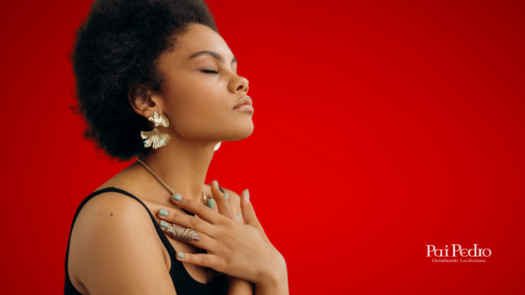 Mulher com olhos fechados e mãos sobre o coração em gesto de conexão e autocompaixão, diante de um fundo vermelho. Sua expressão transmite serenidade, força interior e elevação da energia feminina.