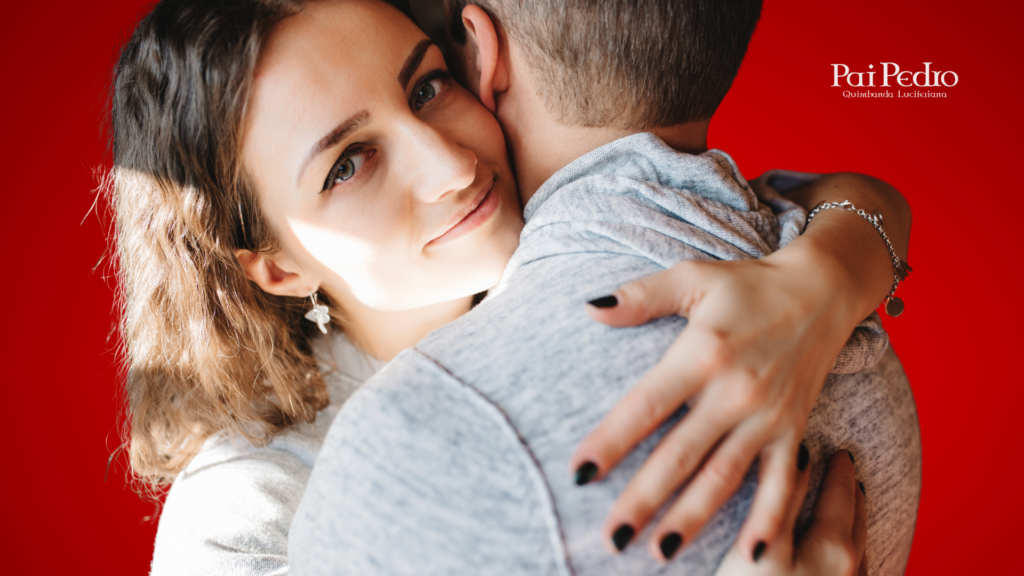 Mulher abraçando um homem com expressão serena e confiante, olhando diretamente para a câmera, simbolizando que o ficante sério virou namorado. O casal veste roupas em tons neutros e o fundo é vermelho vibrante. No canto inferior direito, está o logotipo de Pai Pedro – Quimbanda Luciferiana. 