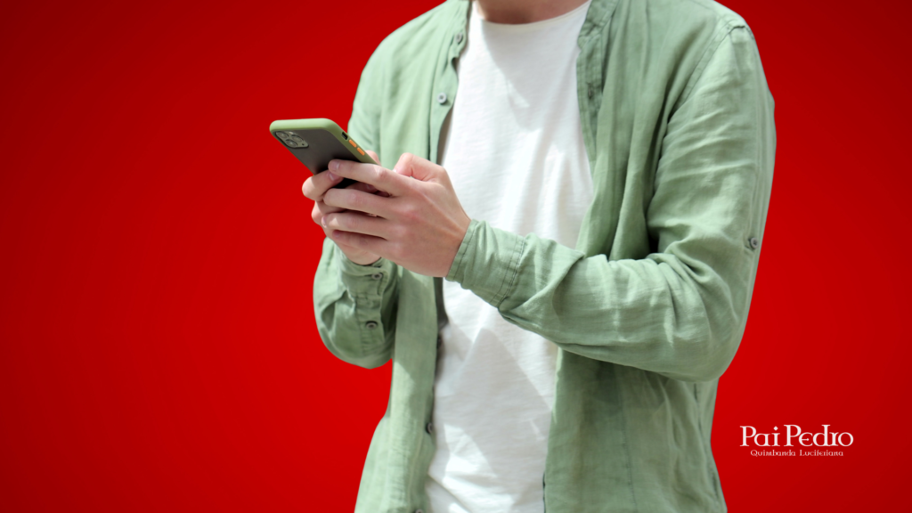 Homem jovem vestindo camisa verde e camiseta branca, concentrado no celular, como quem está mandando uma mensagem carinhosa, se colocando como um ficante sério. Fundo vermelho sólido e, no canto inferior direito, o logo de Pai Pedro – Quimbanda Luciferiana.