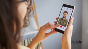 Mulher olhando a tela do celular com foto de um homem sorridente em aplicativo de namoro, representando namoro à distância.